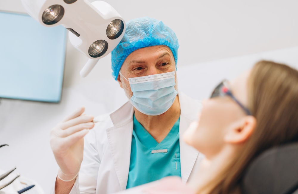 Male dentist in protective mask examining a female patient’s teeth to assess suitability for implants or partial dentures.