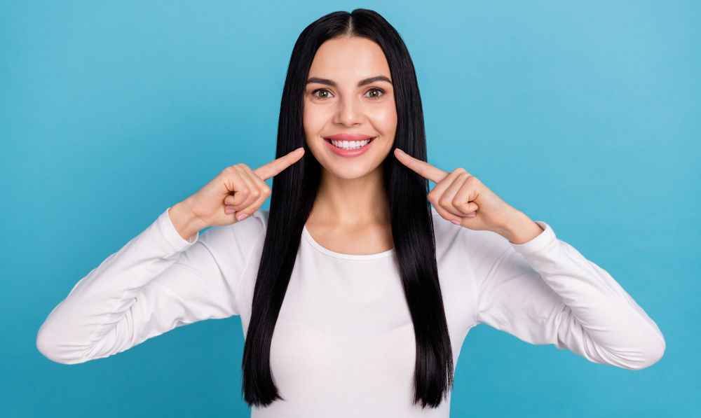A woman pointing to her teeth after dental treatment, showing improved smile alignment following restorative dentistry.